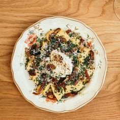 a white plate topped with pasta and an egg on top of it next to a glass of wine