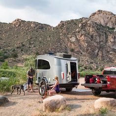 two people and their dog are camping in the mountains with an rv parked next to them