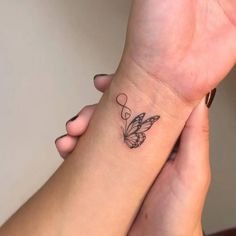 two hands holding each other with tattoos on their wrist and one has a butterfly tattoo on it