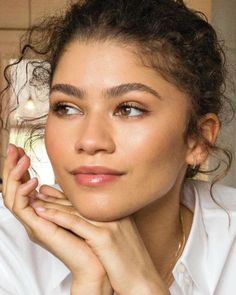 a close up of a person wearing a white shirt and holding her hand near her face