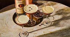 three glasses filled with drinks sitting on top of a table next to bottles and spoons