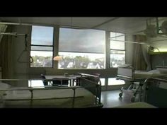 a hospital room filled with lots of beds and medical equipment in front of large windows