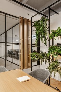 an office with glass walls and plants on the wall, in front of a wooden table