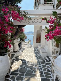 an alley way with flowers and potted plants on either side that leads to the water