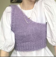 a woman wearing a purple knitted sweater and white shirt with her hands in her pockets