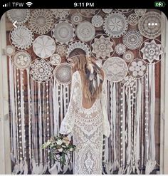 a woman standing in front of a wall covered with white doily and tassels