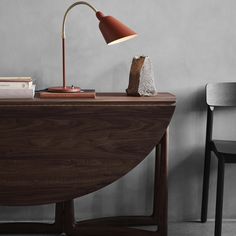 a wooden desk with a lamp on it next to a black chair and a gray wall