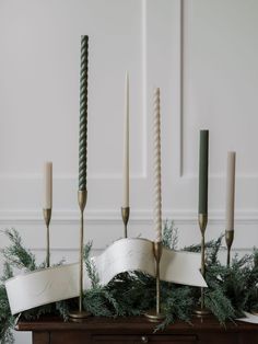 candles are lined up on top of a table with greenery and ribbons around them