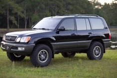 a black suv parked on top of a lush green field next to a lake with trees in the background