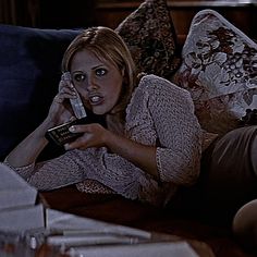 a woman sitting on a couch talking on a cell phone while holding a remote control