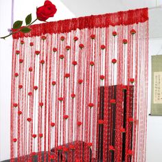 a red curtain with roses hanging from it's side and some string on the wall