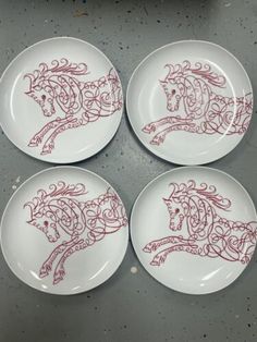 four plates with red designs on them sitting on a gray table top next to a potted plant