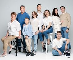 a group of people posing for a family photo in front of a gray background with one person sitting on a chair and the other standing