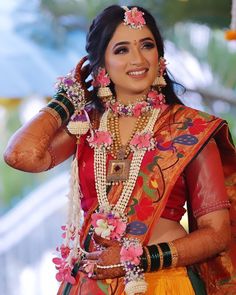 a woman in an orange and yellow sari with flowers on her head is smiling at the camera