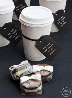 coffee cups with tags on them sitting next to small pieces of chocolate and marshmallows