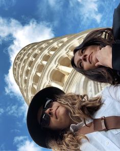 two women standing next to each other in front of a tall building with a sky background