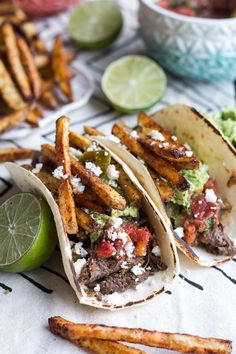 three tacos and some guacamole on a table with other food items