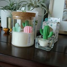 a wooden table topped with two glass jars filled with cactus plants and candles on top of it