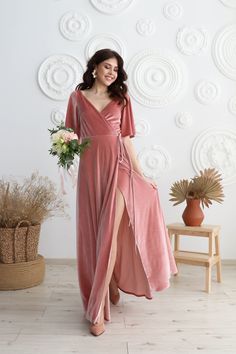 a woman in a pink dress standing next to a vase with flowers on the floor