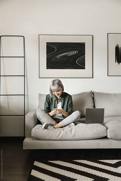 an older woman sitting on a couch using a laptop computer while looking at her cell phone