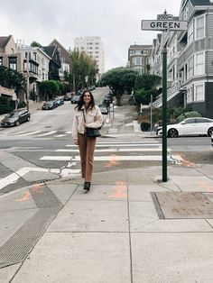 a woman standing on the sidewalk in front of a street sign that says green lane