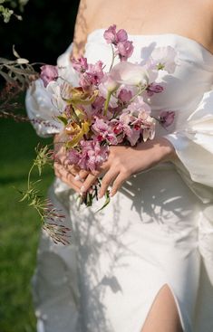 a woman in a white dress holding a bouquet of pink and white flowers on her wedding day