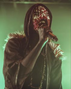 a man wearing a mask and holding a microphone in his hand while standing on stage