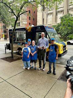 a group of people standing in front of a food truck on a city street next to a tree