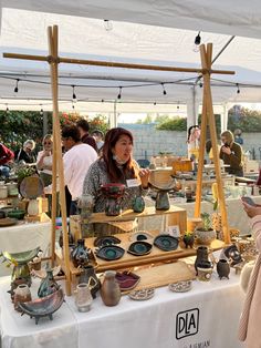 two women are talking to each other in front of a table with pottery on it