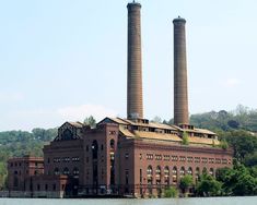 an old brick factory with two towers on the top of it's roof and water in front of it