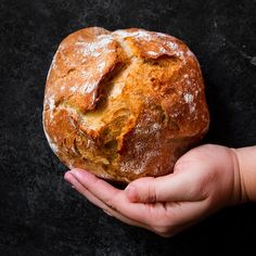 a person holding a loaf of bread in their hand on a black surface with some powdered sugar