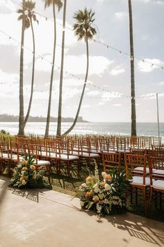 rows of chairs with flowers and greenery in front of palm trees on the beach