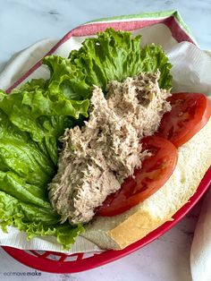 a sandwich with lettuce and tomatoes in a red bowl on a marble table