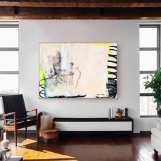 a painting hangs on the wall above a bench in a room with wooden floors and large windows