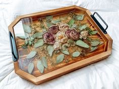 a wooden tray with flowers and leaves on the bottom is sitting on a white sheet