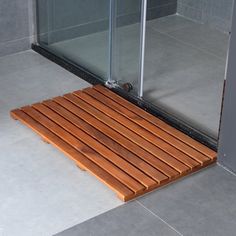 a wooden shower mat in front of a glass door