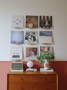 a dresser with pictures on the wall and a potted plant sitting on top of it