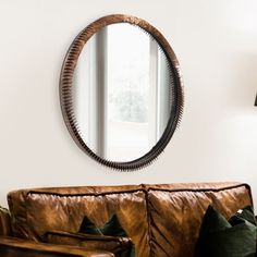 a living room with a brown leather couch and round mirror on the wall