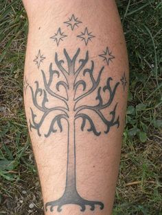 a man's leg with a tree tattoo on it, sitting in the grass