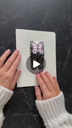 two hands holding a piece of paper with a butterfly on it and the video below