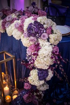 purple and white flowers are arranged in the shape of a heart on a table with candles