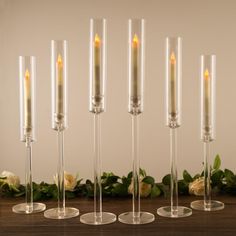 four candles are lined up next to each other on a table with flowers in the background