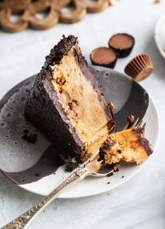 a piece of chocolate cake on a plate with a fork and some cookies in the background