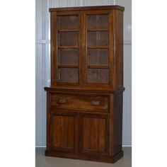 an old wooden china cabinet with glass doors on the top and bottom shelves, in front of a white wall