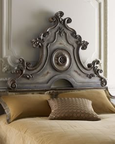 an ornate headboard on a bed in a room with white walls and gold pillows