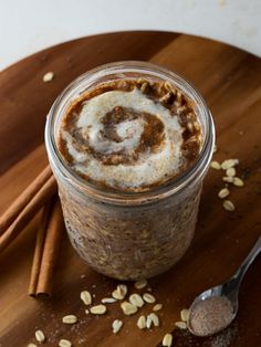 a glass jar filled with cinnamon rolls on top of a wooden cutting board next to two spoons