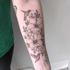 a woman's arm with flowers and a hummingbird tattoo on her left forearm