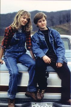 two young people sitting on the back of a pickup truck, posing for a photo