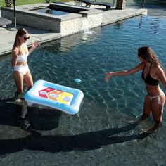 two women in bathing suits are playing with an inflatable pool toy next to a swimming pool