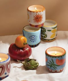 there are many different types of candles on the table with fruit and vegetables next to them